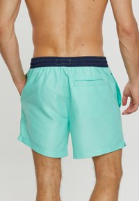 Shorts de bain turquoise avec une taille élastique navy, une poche arrière et une texture lisse. Les shorts ont une coupe droite et des coutures latérales.