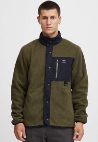 Fleece jacket in olive green with navy accents, featuring a snap closure, zippered chest pocket, and side pockets. Smooth texture with a casual fit.