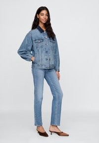 Svetlo modra jeans jakna z temno modrim ovratnikom, ki ima dva sprednja žepa in gumbe za zapenjanje, v kombinaciji s svetlo modrimi oprijetimi kavbojkami.