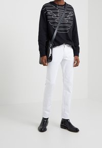 Svart sweatshirt med vit linjeteckning, vita slim-fit jeans och svarta ankellångstövlar. Crossbody-väska i ett texturerat svart material.