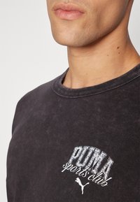 Black cotton sweatshirt with a crew neckline and a faded texture. Features a white printed logo saying "PUMA sports club" on the chest.