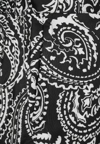 Svart och vitt tyg med ett paisleymönster som har svängar och kurvor; inkluderar en synlig söm och en liten fickdetalj.