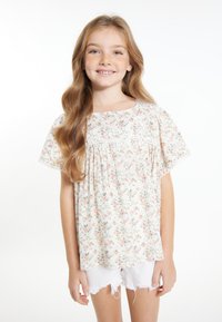 Bluse med kort ærme i blomstertryk, der har en rund halsudskæring, sammensyning på livstykket og blonder trim på ærmerne, parret med hvide slidte shorts.