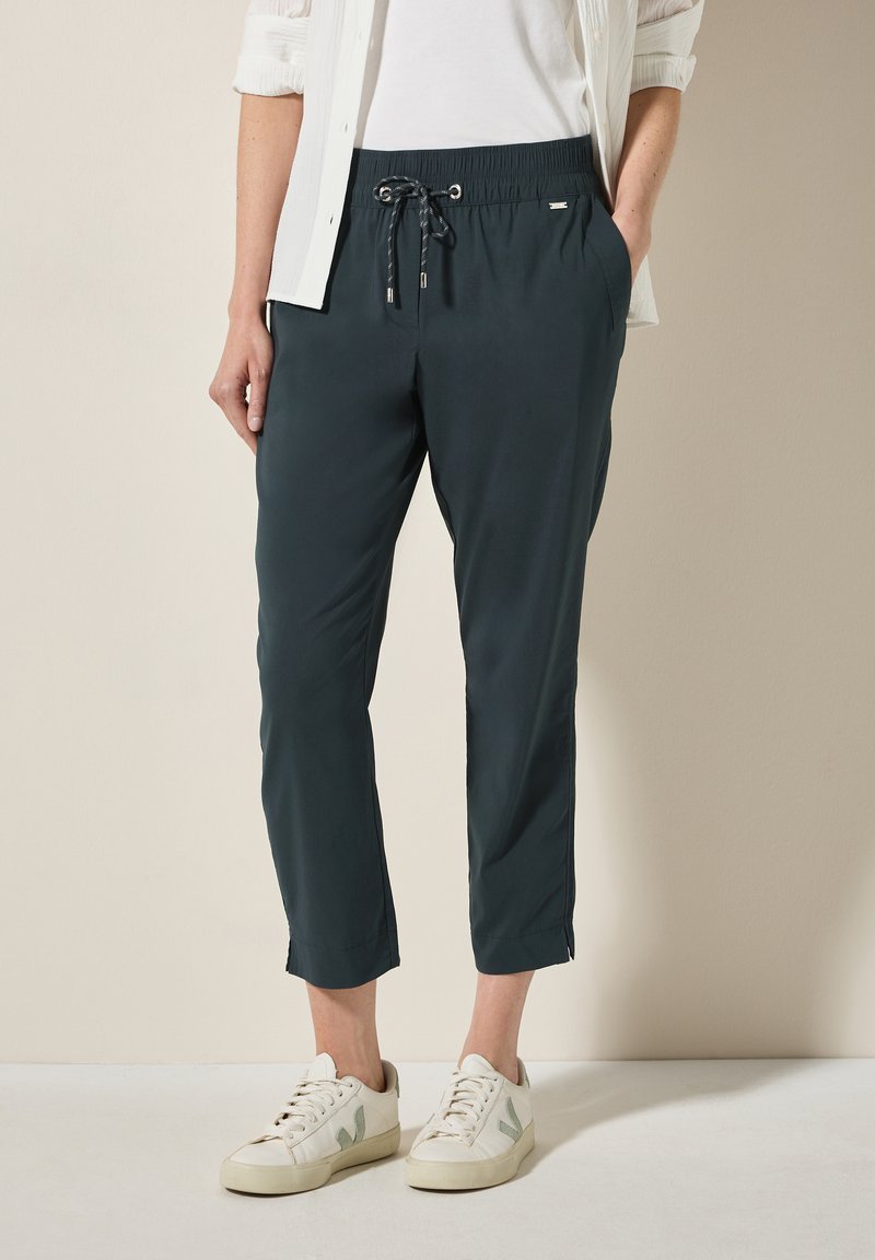 Pantalons cropped vert foncé avec une taille élastique, cordon de serrage ajustable, poches latérales et une texture de tissu lisse et légère.