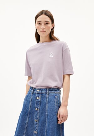 Light lavender cotton t-shirt with a round neckline and short sleeves, featuring an embroidered ribbon detail on the chest, paired with a denim skirt.