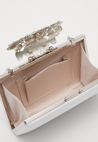Kabelka s ozdobným stříbrným květinovým zapínáním, světle růžovým textilním interiérem a malou vnitřní kapsou.