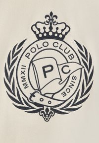 Logo ricamato su uno sfondo crema, con una corona, una corona di alloro e una bandiera con il testo "P.C.", insieme a "Polo Club" e "MMXII."