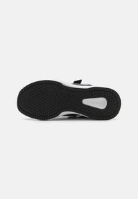 Semelle de sneaker en caoutchouc noir avec un motif de grip texturé, intercalaire blanc et découpe ovale pour une traction optimale. Conçue pour la stabilité et le confort.