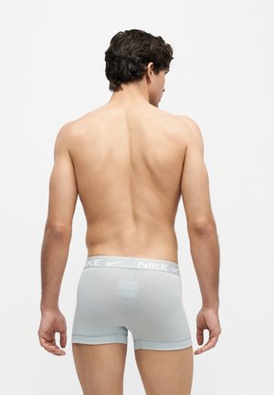 Männliches Modell von hinten, das hellgraue Nike-Boxershorts vor weißem Hintergrund trägt.