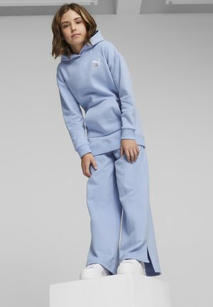 Sudadera azul clara con un bolsillo tipo canguro, combinada con pantalones de pierna ancha a juego, ambos hechos de una tela suave. Se ven zapatos de plataforma blancos.