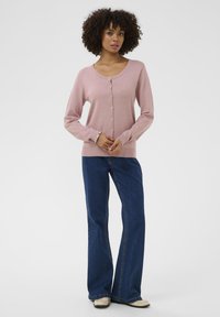 Hellrosa Strickcardigan mit Rundhalsausschnitt, langen Ärmeln und durchgehender Knopfleiste. Kombiniert mit ausgestellten Jeans.