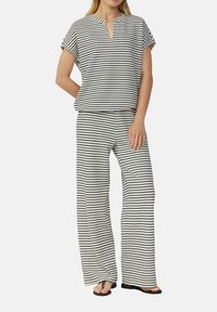 Czarna i biała bluzka w paski z dekoltem w kształcie łezki, zestawiona z szerokimi spodniami w tym samym wzorze. Lekki materiał, luźny krój.