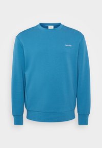 Blauwe sweatshirt van zacht materiaal, met een ronde hals, lange mouwen en een klein wit logo op de borst. Geribbelde manchetten en zoom.