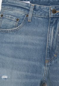 Svijetlo plave traperice s istrošenim detaljima sprijeda, koje imaju bakrenu opremu i klasičan dizajn s pet džepova.