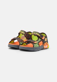 Svarte og oransje sandaler med justerbare stropper, teksturerte grønne detaljer, et smilende dinosaur-motiv og grå gummisåle.