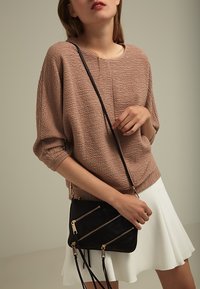 Suéter texturizado rosa claro con hombros caídos, combinado con una falda blanca de corte acampanado. Bolso de hombro negro con bolsillos con cremallera en diagonal.