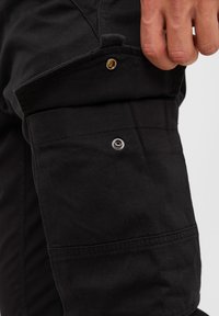 Svarta cargobyxor med en klaffficka med tryckknapp, textil med struktur och synliga sömmar längs sidorna.