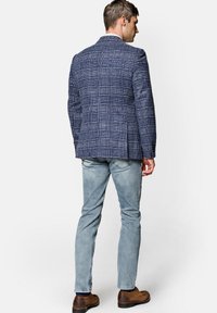 Granatowa marynarka w kratę o dopasowanym kroju, z fakturowanej tkaniny, z pojedynczym rozcięciem z tyłu, w połączeniu z jasnymi dżinsami i brązowymi botkami.