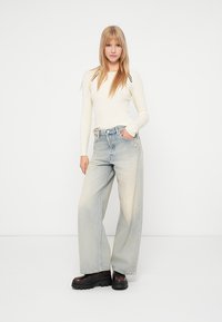 Κρέμα ribbed μπλούζα με μακρύ μανίκι συνδυασμένη με φαρδιά, ανοιχτό μπλε τζιν παντελόνι και χοντρά μαύρα μποτάκια με πλατφόρμα. Απλός σχεδιασμός, κανονική εφαρμογή.