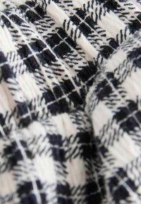 Wollmischgewebe mit einem schwarz-weißen Karomuster, das unterschiedliche Texturen aufweist und eine weiche, leicht flauschige Oberfläche hat.