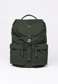 Zaino in tessuto verde con una patta arrotondata, tasche frontali, accessori neri e una maniglia superiore. Presenta un logo minimale sulla parte anteriore.