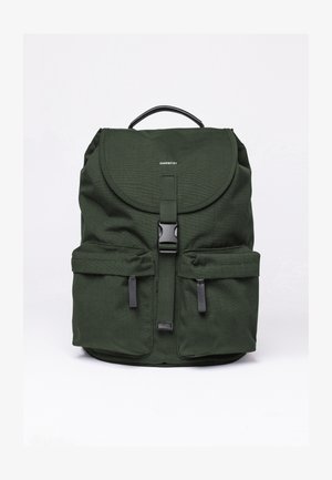 Grüner Stoff-Rucksack mit einer abgerundeten Klappe, Fronttaschen, schwarzem Zubehör und einem Tragegriff oben. Verfügt über ein minimales Logo auf der Vorderseite.