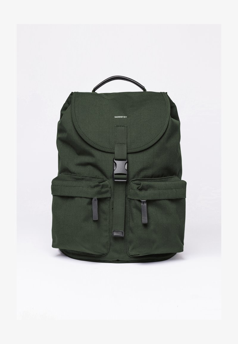 Green fabric backpack with a rounded flap, front pockets, black hardware, and a top handle. Features a minimal logo on the front.