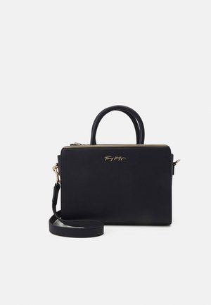 Schwarze rechteckige Handtasche mit zwei Henkeln, abnehmbarem Schulterriemen, goldenem Reißverschluss und goldener Logoschrift vorne in der Mitte.