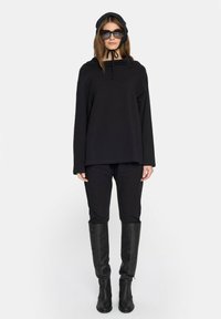 Czarna bluza z kapturem ze sznurkiem, w połączeniu z czarnymi spodniami i czarnymi kozakami do kolan. Czarne okulary przeciwsłoneczne i pasująca czapka dopełniają całość.