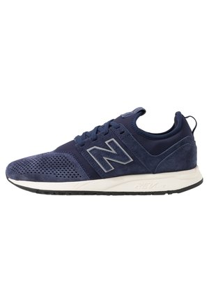 Granatowy sportowy sneaker z perforowanym obszarem palców, szare logo „N” z boku, biała środkowa podeszwa i czarna podeszwa zewnętrzna.