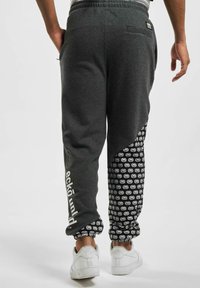Grå sweatpants med en sort mønstret sidelæbe med gentagne grafikker, elastisk talje og sidelommer. Hvidt logo på benet.