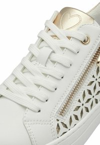 Bílé tenisky se zlatými akcenty, zavazovací design, perforovaný vzor na bocích a dekorační zip. Hladká kožená textura.