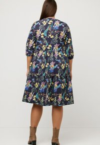Abito floreale con sfondo blu navy, caratterizzato da vivaci motivi di uccelli e fiori, maniche a tre quarti e design a strati della gonna.