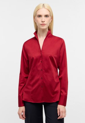Camicia rossa con bottoni, realizzata in tessuto morbido, con colletto alla cinese e maniche lunghe. La camicia ha una vestibilità tailored e una leggera lucentezza.