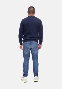 Maglione blu navy, stile aderente, indossato con jeans azzurri chiari, dotati di tasche posteriori, e sneakers bianche con accenti crema.