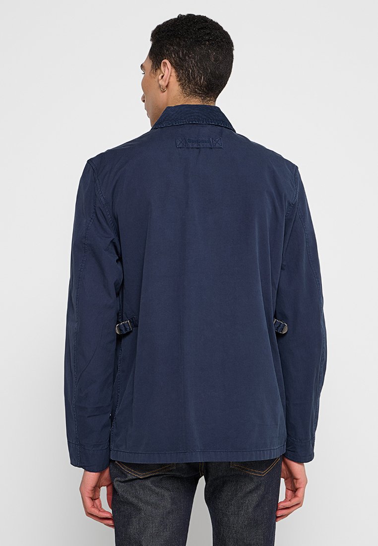 Giacca blu navy, tessuto leggero, fit rilassato, cuciture posteriori visibili, cinturini laterali regolabili, collo classico, design semplice, senza motivi.