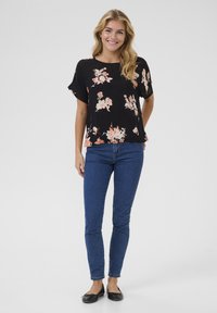 Black floral blouse with short sleeves, featuring pink and cream flowers. Paired with blue skinny jeans and black ballet flats.