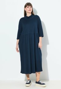 Navy sininen midi-mekko, jossa on kaula-aukko, kolme neljännesosahihnaa ja rypytetty vyötärö. Valmistettu pehmeästä kankaasta, jossa on rento istuvuus.