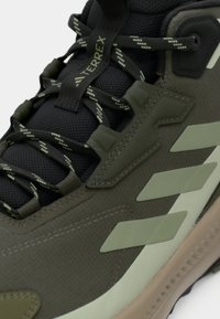 Dunkelgrüner Sneaker mit strukturiertem Stoff, einer festen Gummisohle, einem gepolsterten Kragen und kontrastierenden hellgrünen Akzenten am Obermaterial.