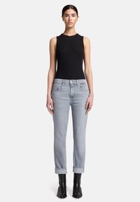 Un débardeur noir à côtes associé à un jean gris clair à revers et des bottines noires. Design simple avec une silhouette ajustée.