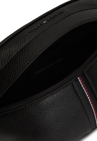 Μαύρη δερμάτινη τσάντα με υφή, που διαθέτει φερμουάρ και ριγέ διακοσμητικό σε κόκκινο, άσπρο και μπλε. Ορατή εσωτερική ετικέτα με το λογότυπο του κατασκευαστή.