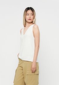 White sleeveless top with a V-neck design, made from a textured fabric, paired with khaki cargo pants featuring side pockets.