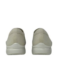 Zapatillas deportivas beige con un upper texturizado, diseño minimalista, talón elástico y suelas de goma con patrones acanalados.