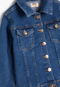 Chaqueta de denim en azul medio con un diseño clásico, que incluye botones plateados, dos bolsillos en el pecho y detalles de costura en color naranja.