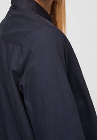 Mörkblå skjorta med krage, slät textur, långa ärmar och knapprader, visad från sidan för att framhäva passform och drapering.