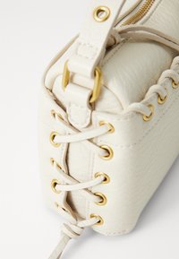 Borsa a mano in pelle bianca con dettagli in oro e lacci laterali. Texture liscia con una forma strutturata, chiusura superiore con cerniera.
