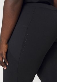 Leggings elásticos negros con un bolsillo lateral y un detalle de pequeños puntos brillantes a lo largo de la costura. Textura suave y diseño ajustado.