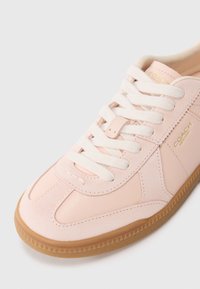 Sneaker in pelle rosa chiaro con pannelli lisci e texture. Presenta lacci bianchi, marchio dorato e suola in gomma naturale con tasselli a forma triangolare.