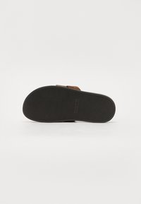 Sandalo a scivolo in suede marrone con suola in gomma nera. Fondo testurizzato per grip e impronta con la scritta "Steve Madden". Design piatto e aperto all'altezza delle dita.