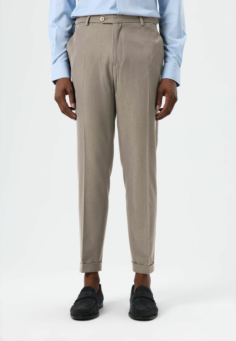 Beige maßgeschneiderte Hose mit dezentem Glanz, geradem Schnitt, umgeschlagenen Bündchen und Knopfverschluss, kombiniert mit schwarzen Slippern.